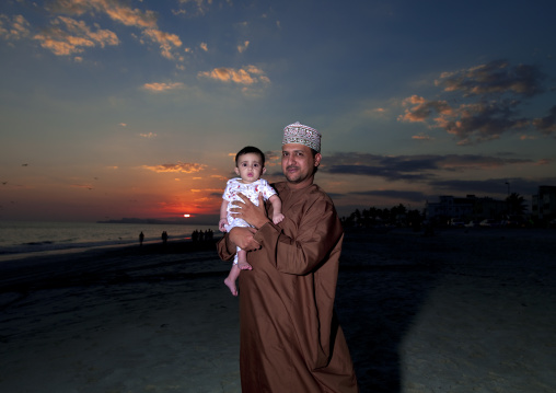 Man Holding His Baby Standing On The Beach At Dusk, Salalah, Oman