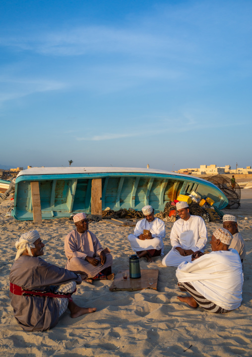 Omani men resting and drinking tea on the beach at sunset, Dhofar Governorate, Mirbat, Oman