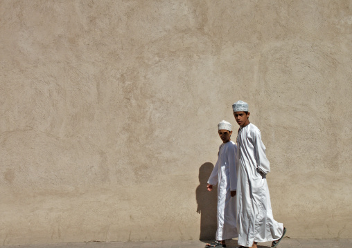 Two Kids In White Dishdasha Passing By Nizwa Fort Wall, Oman