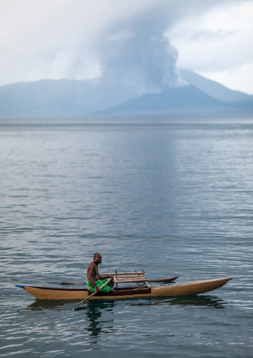 Man on a canoe in front of a volcanic eruption in Tavurvur volcano, East New Britain Province, Rabaul, Papua New Guinea