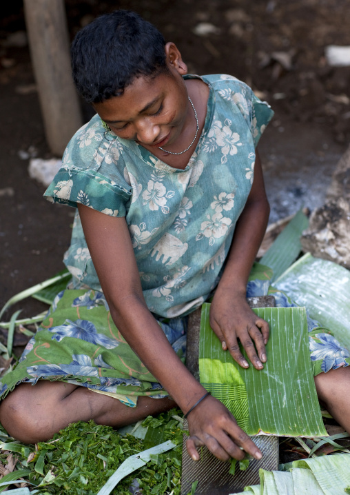 Girl making Doba traditional money with banana leaves on a wooden board, Milne Bay Province, Trobriand Island, Papua New Guinea