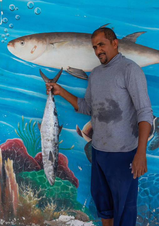Portrait of faranasi man with a big fish in his hand in front of a mural painting, Red Sea, Farasan, Saudi Arabia