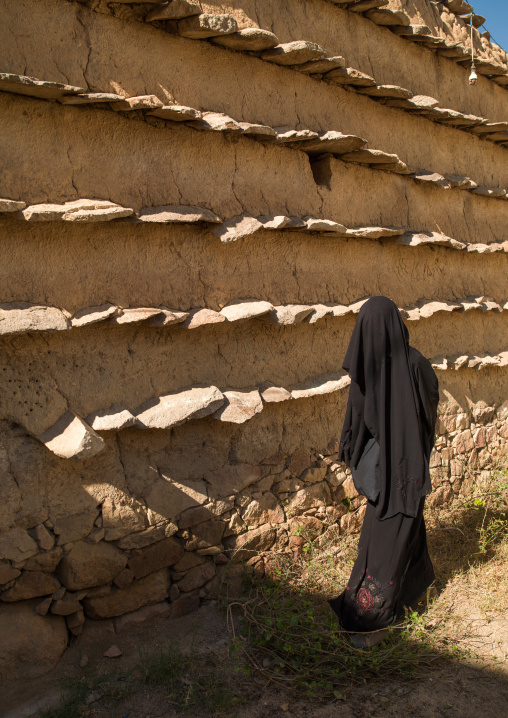 Saudi woman in front of traditional clay and silt homes in a village, Asir Province, Ahad Rafidah, Saudi Arabia