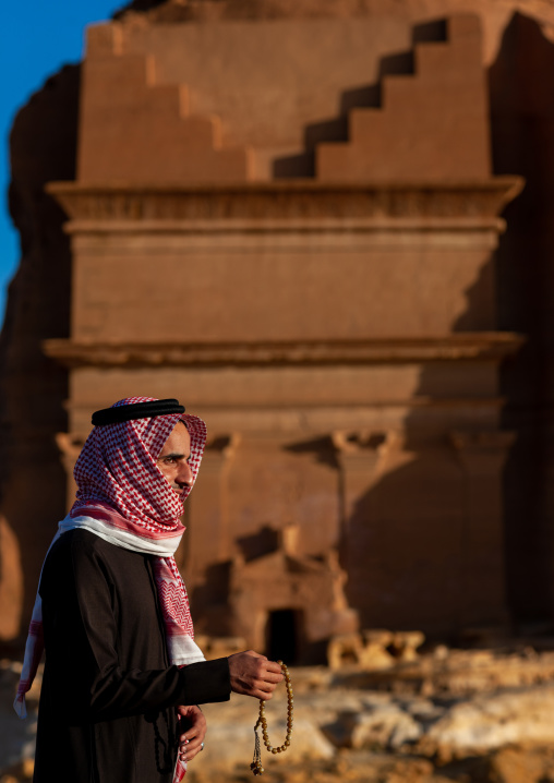 Saudi tourist praying in front of a nabataean tomb in madain saleh archaeologic site, Al Madinah Province, Al-Ula, Saudi Arabia