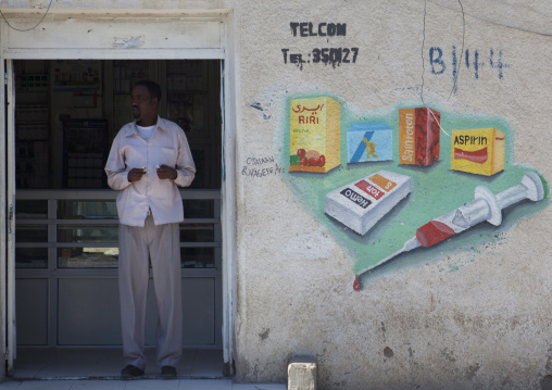 A Man Standing Inside A Medical Dispensary With Painted Advertisment Onto The Wall, Boorama, Somaliland