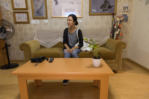 South Korean visitor sit on a sofa during the exhibition Pyongyang sallim at architecture biennale showing a north Korean apartment replica, National Capital Area, Seoul, South Korea
