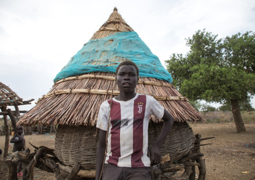Toposa tribe boy with a Juventus football shirt standing near a granary, Namorunyang State, Kapoeta, South Sudan
