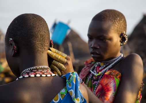 Toposa tribe woman with huge rings putting earrings to a friend, Namorunyang State, Kapoeta, South Sudan