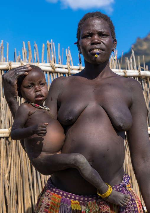 Larim tribe woman carrying her baby in front of a fence, Boya Mountains, Imatong, South Sudan