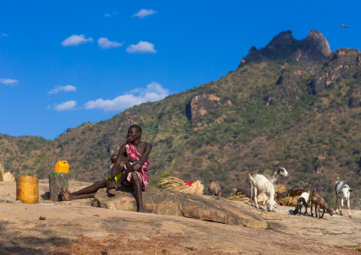 Larim tribe woman sit on a rock in front of the hills, Boya Mountains, Imatong, South Sudan