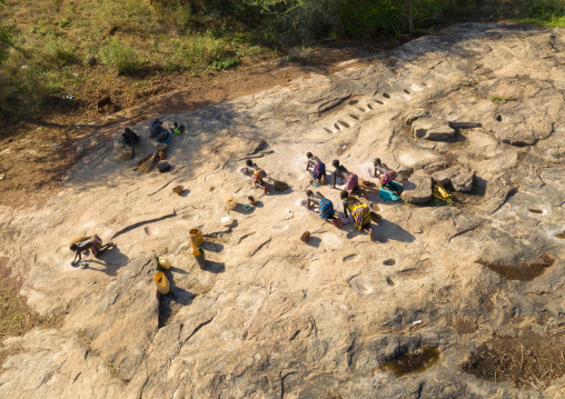 Larim tribe women grinding sorghum grains in holes in a rock, Boya Mountains, Imatong, South Sudan