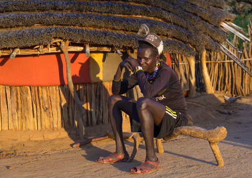 Man sit on a wooden bench in front of a Larim tribe traditional house, Boya Mountains, Imatong, South Sudan