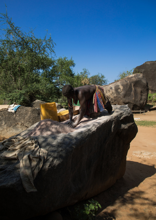 Larim tribe woman grinding grains in a hole in the rock, Boya Mountains, Imatong, South Sudan