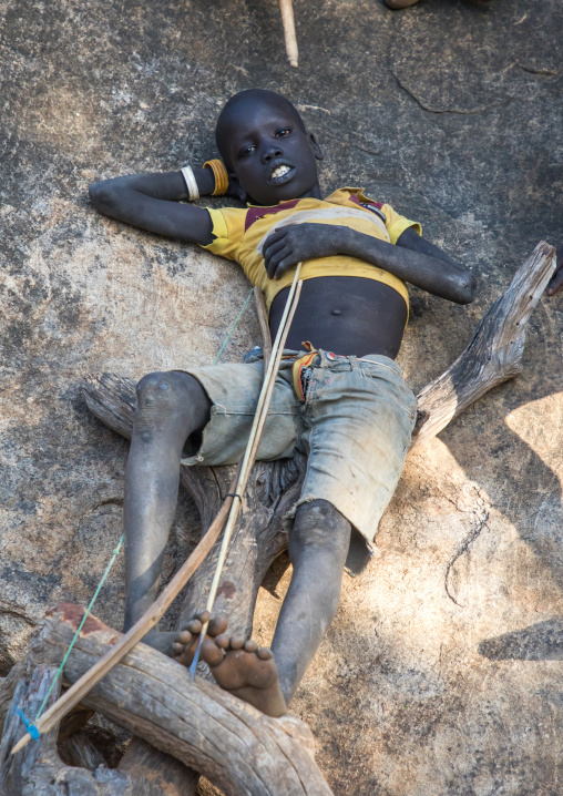 Larim tribe boy with a bow resting on a rock, Boya Mountains, Imatong, South Sudan