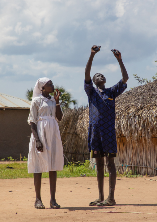 Mundari tribe man with a nun trying to catch a network on mobile phones, Central Equatoria, Terekeka, South Sudan