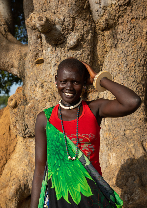 Portrait of a smiling Mundari tribe woman in front of a tree, Central Equatoria, Terekeka, South Sudan