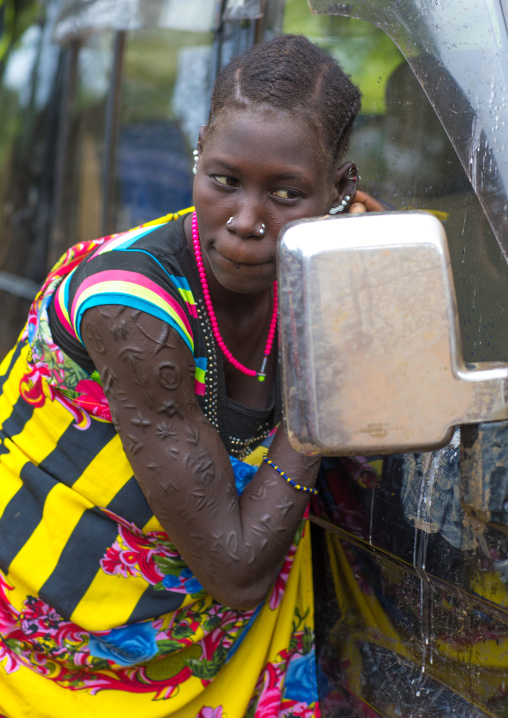 Larim tribe woman with scarifications on her arm looking at herself in a car mirror, Boya Mountains, Imatong, South Sudan
