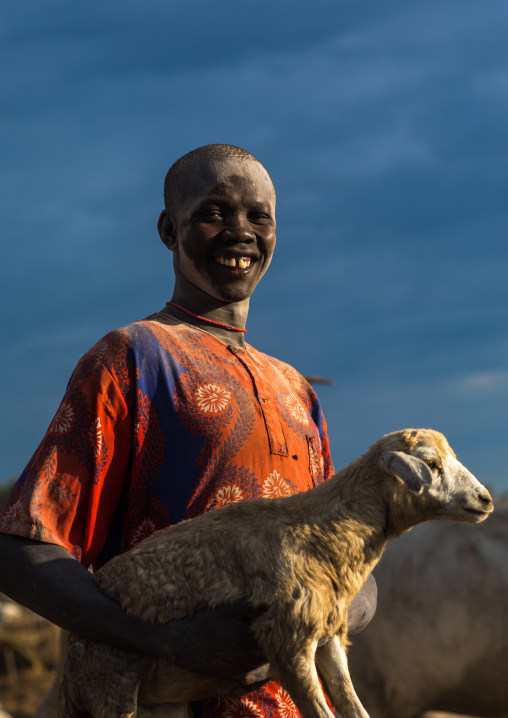 Portrait of a smiling Mundari tribe man carrying a young sheep, Central Equatoria, Terekeka, South Sudan