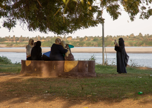 Girl with digital tablet photographing friends in front of the river Nile, Northern State, Al-Khandaq, Sudan
