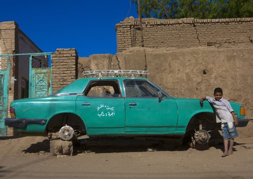 Sudan, Northern Province, Dongola, boy in front of an old green car