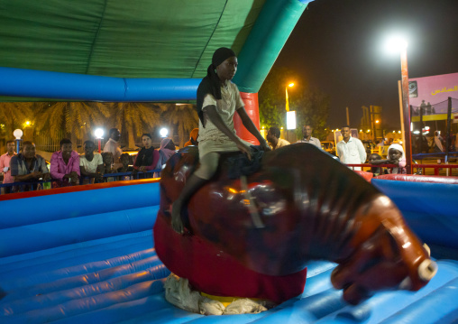 Sudan, Red Sea State, Port Sudan, girl riding a bull in a fun fair