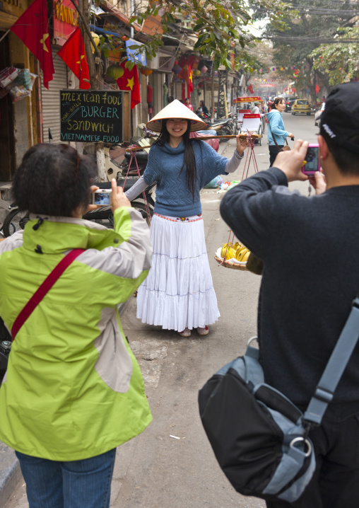 Couple of tourists taking a picture of a woman with a sedge hat, Hanoi, Vietnam