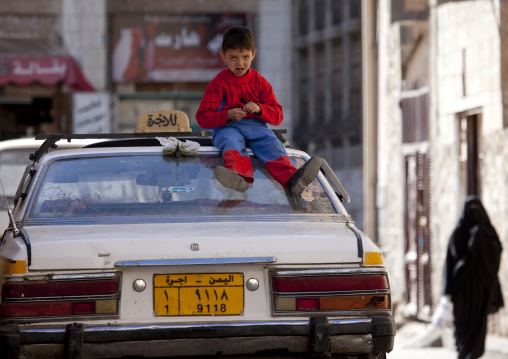 Kid Wearing A Spiderman Suit Sitting On The Top A Car In A Street Of Sanaa, Yemen