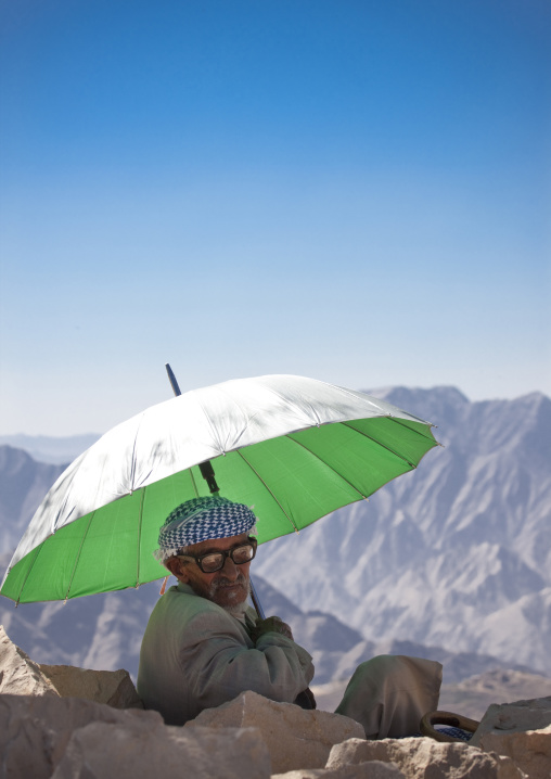 Old Man With Glasses Sitting Under The Shade Of A Green Umbrella In The Mountain, Hababa, Yemen