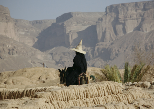 Woman Wearing A Tall Cone Hat And Riding On A Donkey In Rocky Land, Hadramaut, Yemen