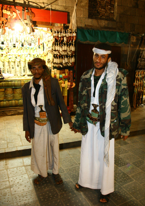 Two Men Wearing Jambiya Hold Hands In Front Of A Jambiya Shop, Sanaa, Yemen