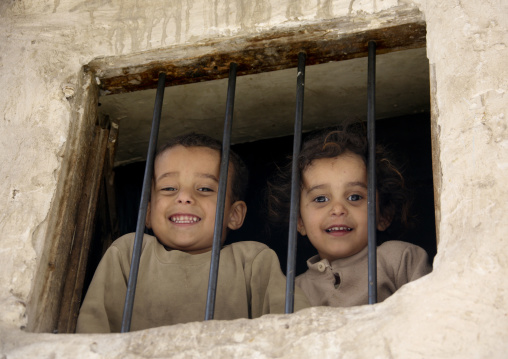 Children With Toothy Smiles Looking Down The Street Through A Window, Sanaa, Yemen