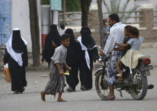 Street Scene, With Fully Veiled Women Walking And A Father Driving His Two Kids On A Motorbike, Zabid, Yemen