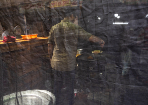 Bangladeshi man cooking hidden behind a curtain during ramadan fast, Dhaka Division, Dhaka, Bangladesh
