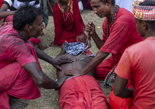Men putting a hook in the back of a man for a body suspension in Charak Puja, Sylhet Division, Kamalganj, Bangladesh