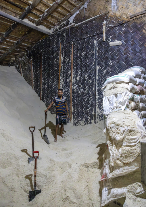 Bangladeshi man picks up salt with a shovel in a warehouse, Chittagong Division, Chittagong, Bangladesh