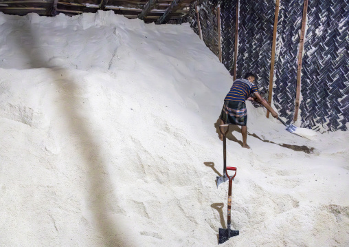 Bangladeshi man picks up salt with a shovel in a warehouse, Chittagong Division, Chittagong, Bangladesh