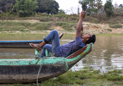 Bangladeshi man taking a selfie lying on a boat, Chittagong Division, Rowangchhari, Bangladesh