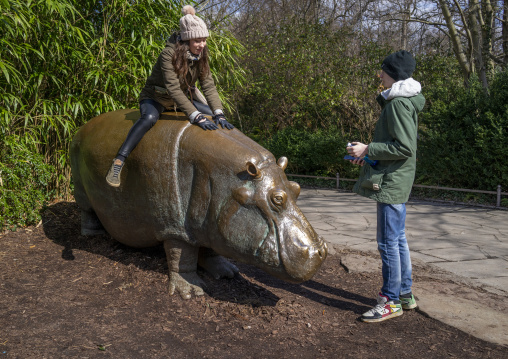 Girl riding Knautschke the hippopotamus bronze statue in Berlin Zoo, Berlin state, Berlin, Germany