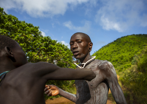 Shepherd from suri tribe receiving help to paint his body, Tulgit, Omo valley, Ethiopia