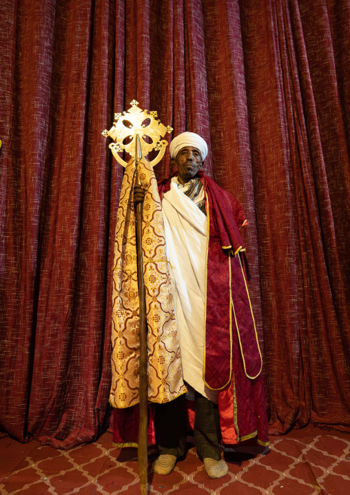 Ethiopian orthodox priest holding a cross inside a rock-hewn church, Amhara Region, Lalibela, Ethiopia