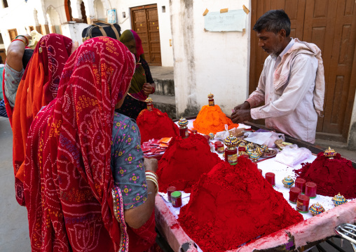 Indian man selling red colored powders to women, Rajasthan, Pushkar, India