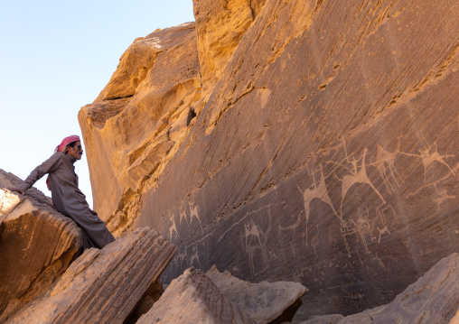 Saudi man in front of petroglyphs on a rock depicting hunters riding horses, Najran Province, Thar, Saudi Arabia