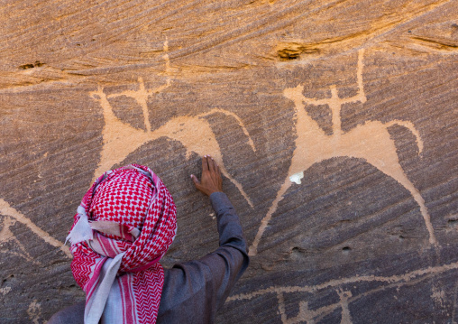 Saudi man in front of petroglyphs on a rock depicting hunters riding horses, Najran Province, Thar, Saudi Arabia