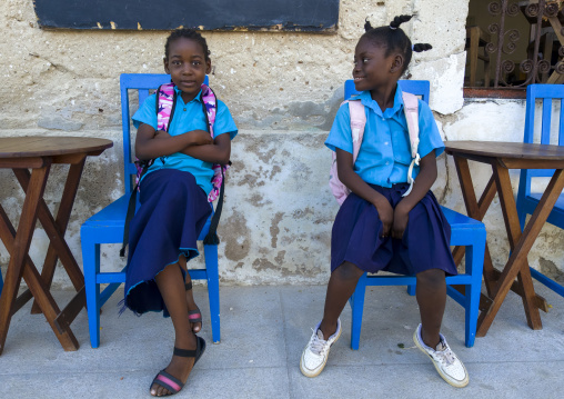 Portrait of two schoolgirls sit on blue chairs, Nampula Province, Island of Mozambique, Mozambique