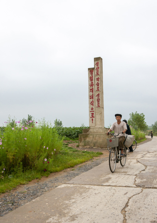 People riding a bicycle in front of a stele about anti japanese guerilla, North Hwanghae, Kaesong, North Korea
