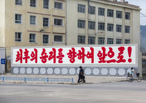 People passing in front of a propaganda slogan about final victory, North Hwanghae, Kaesong, North Korea
