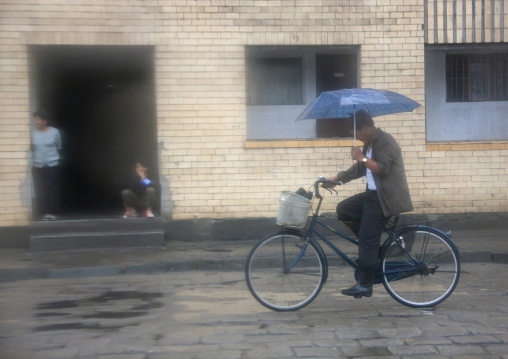 North Korean man riding a bicycle under the rain, South Hamgyong, Hamhung, North Korea