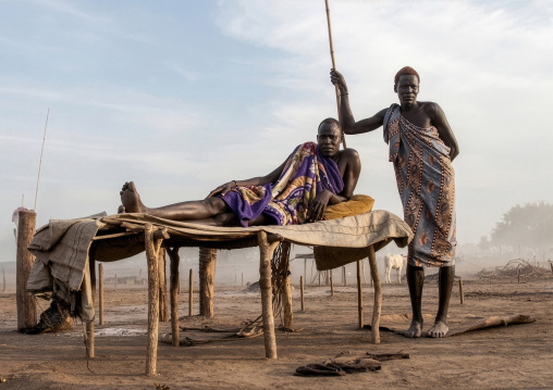 Mundari tribe man resting on a wooden bed in the middle of his cows, Central Equatoria, Terekeka, South Sudan