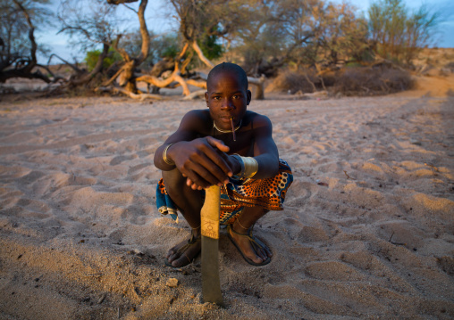 Mucubal tribe man with his machete sit in a dry river, Namibe Province, Virei, Angola
