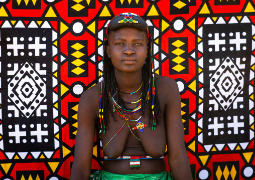 Portrait of a muhakaona tribe woman in front of a colorful printed cloth, Cunene Province, Oncocua, Angola